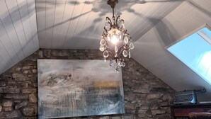 Un accogliente sottotetto adibito a camera da letto, con soffitto spiovente, un lampadario, una parete in pietra, un quadro di grandi dimensioni, un tappeto in pelle di vacca e una macchina da scrivere vintage.