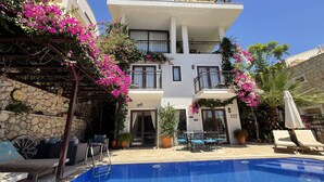 A two-story building with a swimming pool, outdoor seating, and potted plants. - Luxury Villa, Private Pool, Beautiful Gardens, Stunning Sea & Mountain Views (Kalkan)
