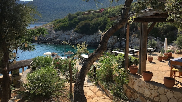 A coastal outdoor seating area with stone walls, potted plants, and umbrellas. - Luxury Villa, Private Pool, Beautiful Gardens, Stunning Sea & Mountain Views (Kalkan)