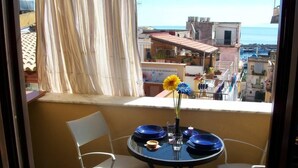 Een balkon met een tafel gedekt voor twee personen, blauw servies en een bloevas.