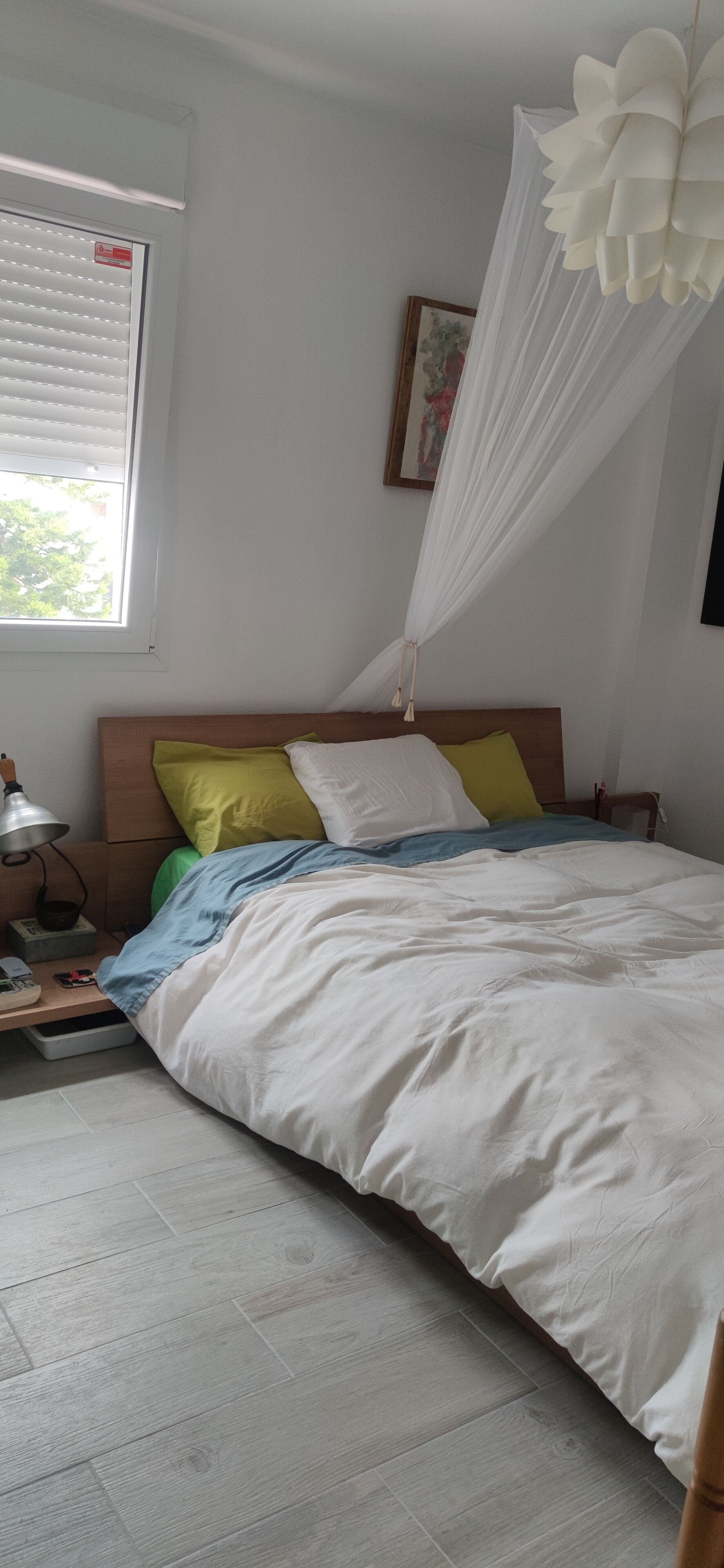 Une chambre à coucher avec un lit, une table de chevet, une lampe et une fenêtre avec des stores.