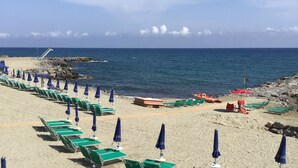 Una playa con filas de sillas reclinables verdes y sombrillas azules, dispuestas a lo largo de la orilla.