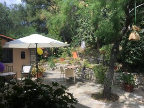 Une terrasse extérieure avec un sol en pierre, entourée de plantes en pot et d’un mur de pierre.