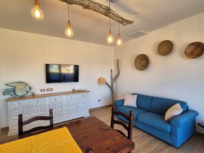 Ein Wohnzimmer mit blauem Sofa, einem Holzesstisch und einem an der Wand befestigten Fernseher.