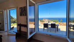 A room with a large sliding glass door leading to an outdoor patio with a table and chairs, a stone wall, and a view of the ocean. - House in the countryside with wonderful views Asinara Gulf and Castelsardo (Castelsardo)