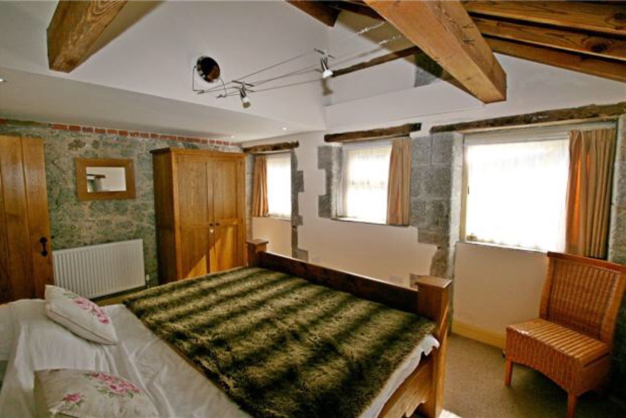 Ein Schlafzimmer mit Bett, Holzmöbeln, einem Fenster mit Vorhängen und einer Heizung.