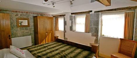 Ein Schlafzimmer mit Bett, Holzmöbeln, einem Fenster mit Vorhängen und einer Heizung.