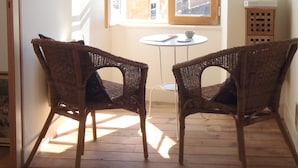 A room with two wicker chairs facing a small round table, a window with an open shutter, and a white wall. - Fisherman's Cottage with WiFi and views to the harbour. (Mortagne-Sur-Gironde)
