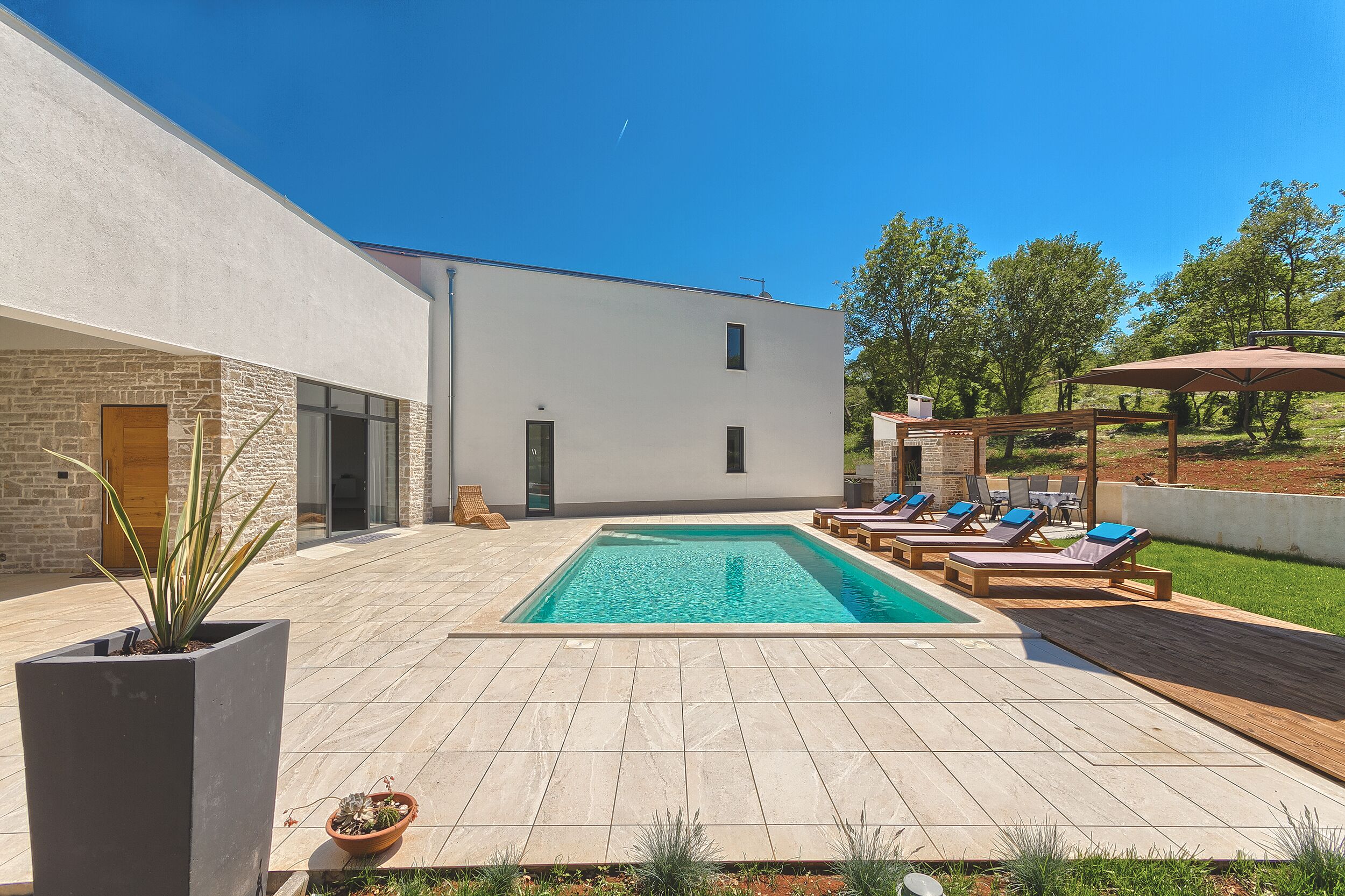 A modern outdoor pool area with a rectangular pool, lounge chairs, and a pergola.