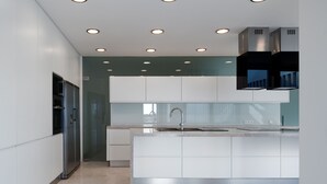 Una cucina moderna con faretti a soffitto, un frigorifero in acciaio inossidabile, mobili bianchi e un'isola centrale con lavello.