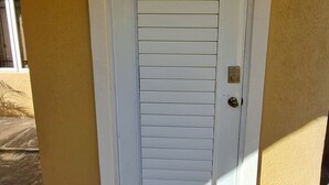 Eine weiße Tür mit horizontalen Lamellen, ein kleines Fenster darüber und die Zahl '2' an der rechten Wand.