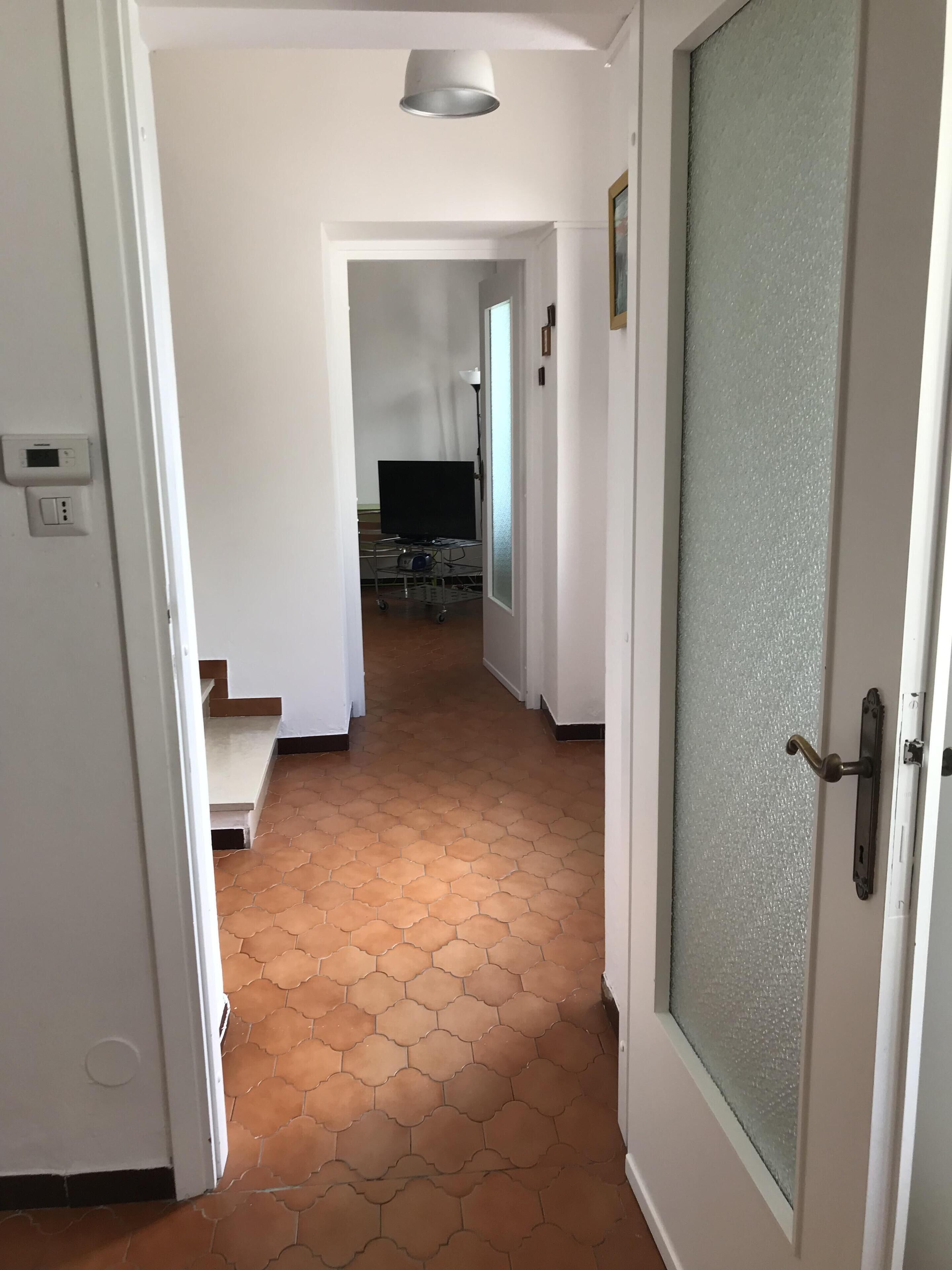 A hallway with a tiled floor, a door with a frosted glass panel, and a ceiling light fixture.