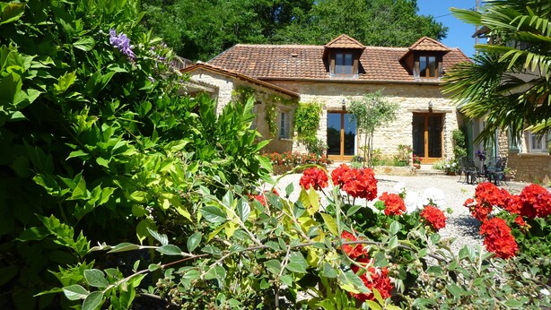 A stone house with a tiled roof, surrounded by lush greenery and flowering plants. - Beautiful retreat With Panoramic Countryside Views close to Hautefort Chateau. (Hautefort)