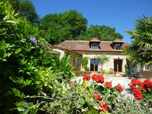 A stone house with a tiled roof, surrounded by lush greenery and flowering plants. - Beautiful retreat With Panoramic Countryside Views close to Hautefort Chateau. (Hautefort)