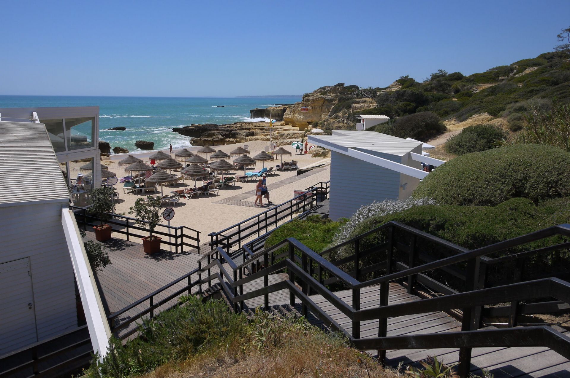 Ein Strandhotel mit Holzterrasse, Strandstühlen und Sonnenschirmen.