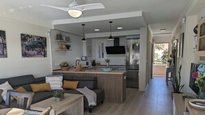 A modern living room with a sofa, coffee table, and dining area. A kitchen with a refrigerator and microwave is visible in the background. -  TORREMAR APARTMENT IN FRONT OF THE SEA.  VT- 450557-A (ALICANTE/ALACANT)