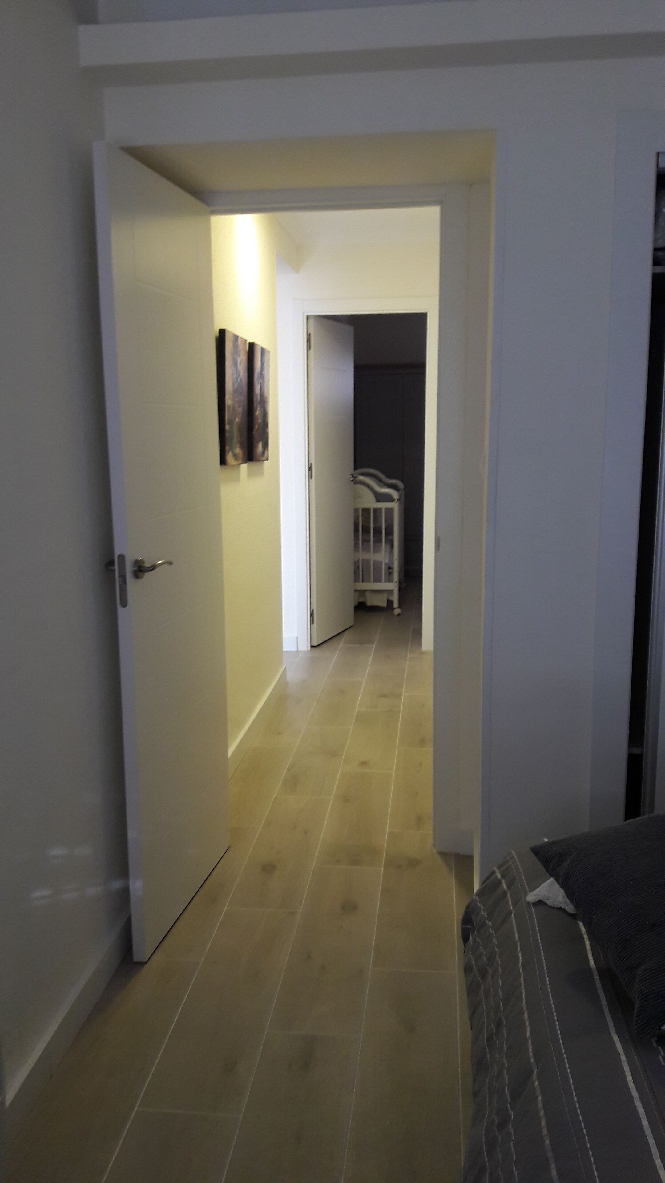A narrow hallway with a door on the left, a white crib in the center, and a bed on the right.