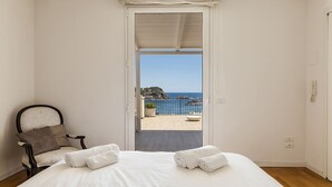A bedroom with a bed, a chair, and a view of the sea through an open door.