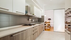 A modern kitchen with grey tiles, wooden cabinets, stainless steel appliances, and a dining area with a table and chairs.