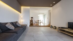 A modern living room with a grey sofa, a TV, and a dining area with chairs and a table.