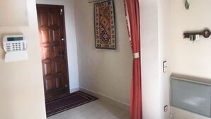 Un couloir avec une porte en bois, une décoration murale à motifs, un rideau rouge, un clavier de sécurité et un radiateur.