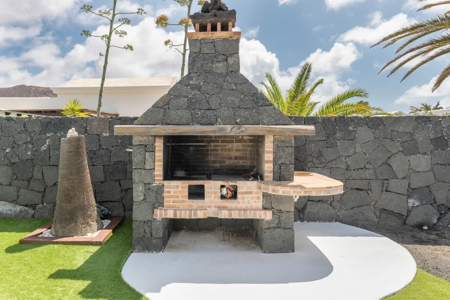 A stone-built outdoor kitchen with a chimney, a flat grill area, and a small seating space.