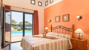 Une chambre à coucher avec un lit, une table de chevet, une lampe, une fenêtre et une vue sur une piscine.