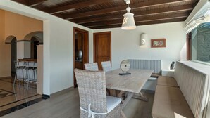 Un coin repas avec un plafond en bois, une table entourée de chaises en osier et un banc.