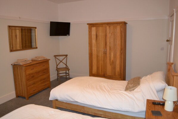 A bedroom with a bed, a wooden wardrobe, a television mounted on the wall, and a bedside table with a lamp.