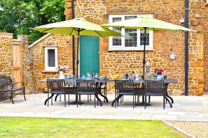 An outdoor patio with a stone wall, a table set with chairs, and two green umbrellas.