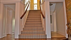 A grand staircase with a striped carpet, wooden handrails, and a decorative sculpture at the bottom. - Large house with sea views, ample off-road parking, enclosed garden with terrace (Hunstanton)