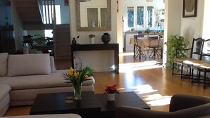 A living room with a sofa, a coffee table with a vase of flowers, and a dining area with chairs and a table.