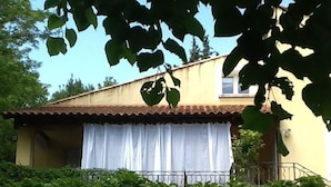 A two-story house with a balcony, a red umbrella, and a stone archway leading to a patio area.