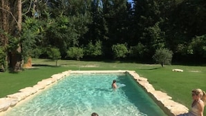 A rectangular swimming pool with clear water, surrounded by a stone border.