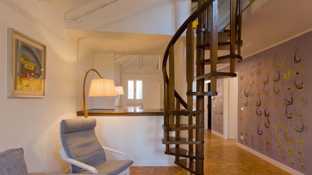 Een modern interieur met een houten wenteltrap, een witte stoel en een wand met ophanghaken.