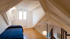 Een kleine zolderkamer met houten vloer, een bed, een radiator en een raam.