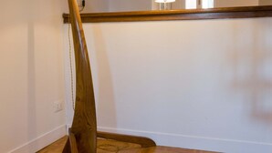 Een hoek van een kamer met een houten vloer, een lamp met een witte kap en een uitzicht op een raam en een deur op de achtergrond.