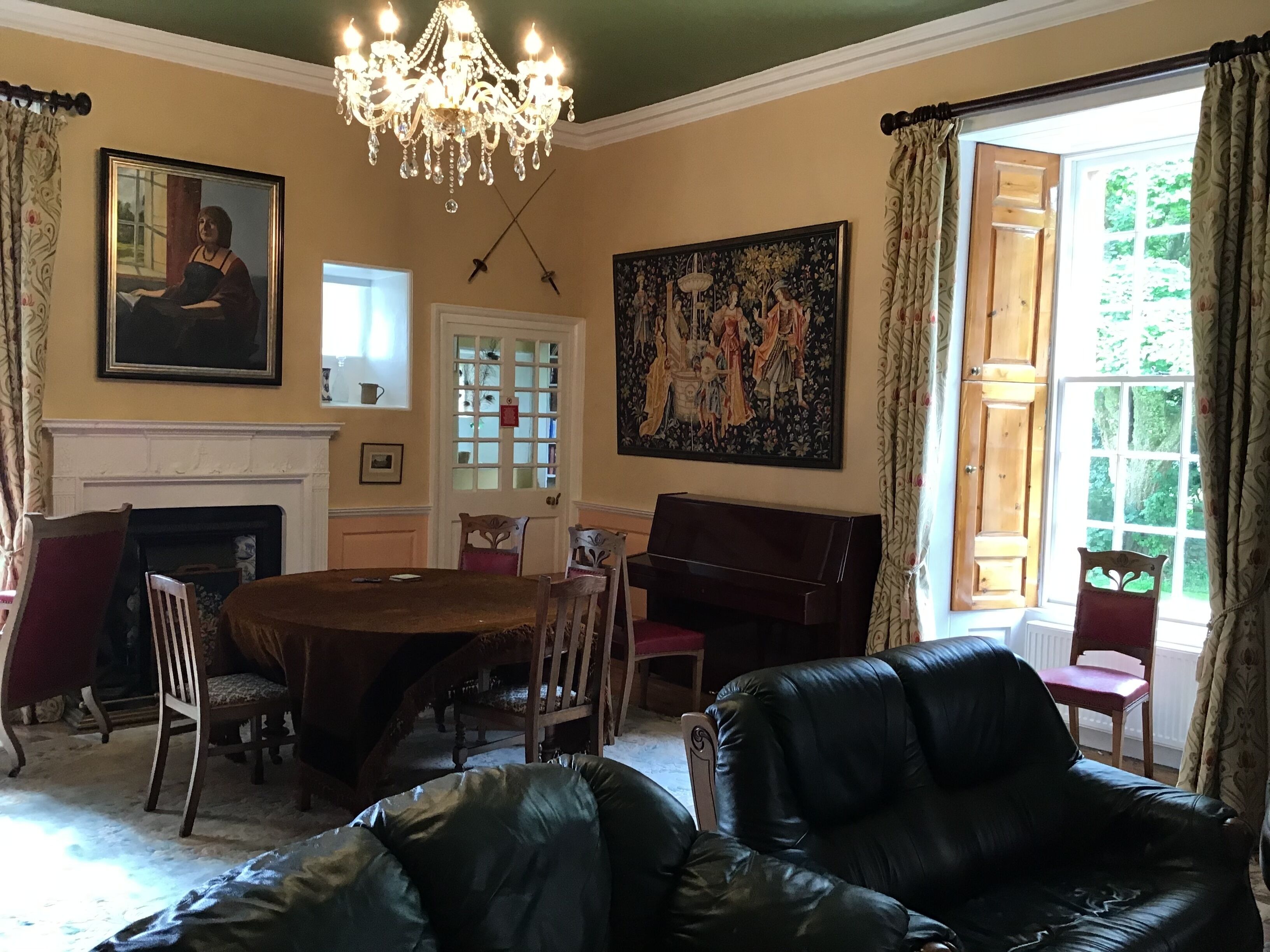 A dining room with a chandelier, a fireplace, a piano, and a large painting.