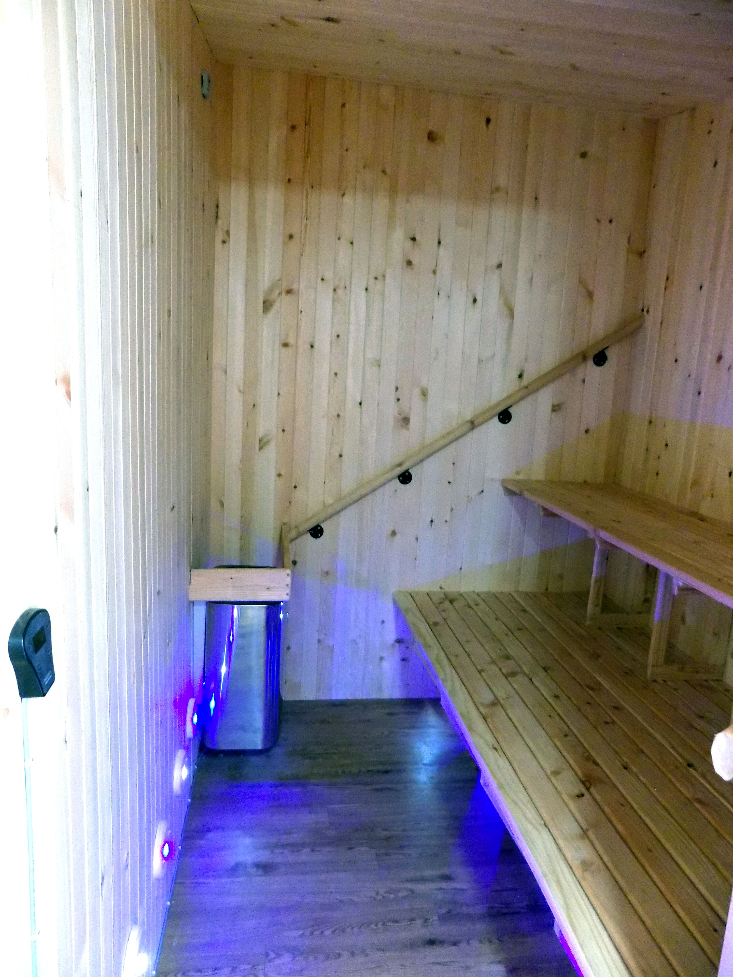 Interior de madera con techo inclinado, un banco de madera y un cubo de basura pequeño.