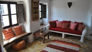 A cozy living room with a stone floor, a red sofa with patterned cushions, a wooden bench, and a small table. - Beautiful Farmhouse, Private Pool, Stunning Views Free Wifi, Historic Montefrio (Montefrio)