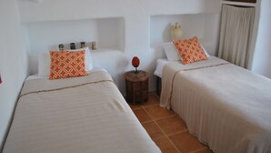 A room with two beds, each with a white and orange patterned pillow, a small wooden nightstand with a red decorative item, and a white vase on the wall. - Beautiful Farmhouse, Private Pool, Stunning Views Free Wifi, Historic Montefrio (Montefrio)
