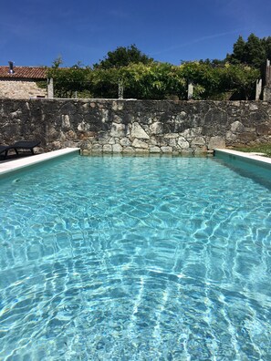 A clear swimming pool with stone walls and a tiled roof.