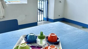 Ein Balkon mit Blick auf den Ozean, ein Tisch mit bunten Teekannen und ein blauer Geländer.
