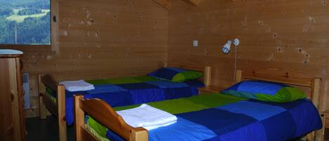 Une chambre dans un chalet en bois, avec deux lits, une fenêtre et une armoire en bois.