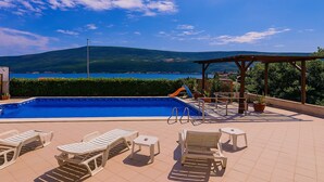 Une piscine dotée de chaises longues et d’une pergola offrant une vue panoramique.