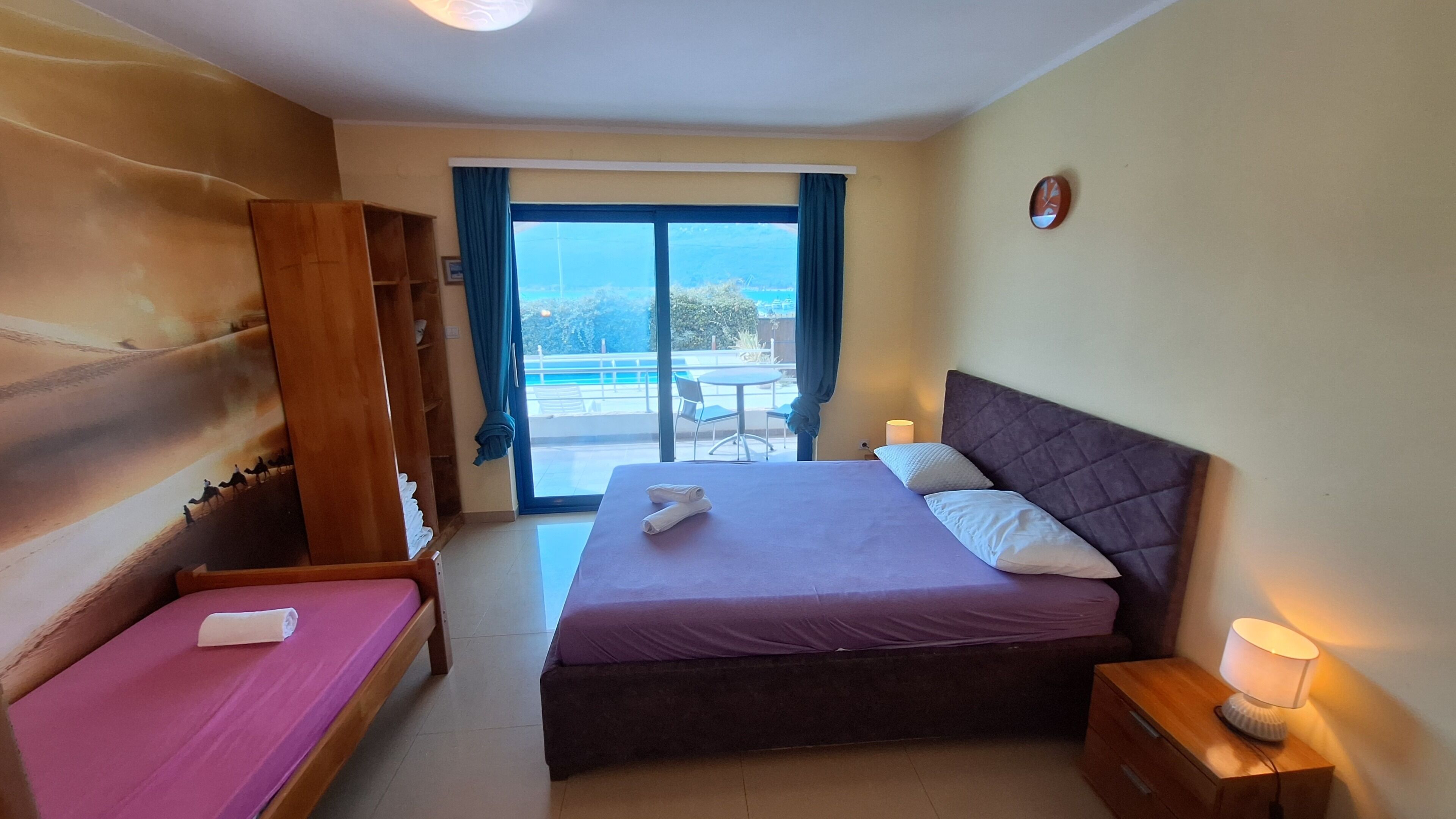 Habitación de hotel con cama, una mesita, mesita de noche, armario y vistas al exterior.