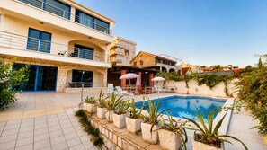 A multi-story building with a swimming pool, outdoor seating, and potted plants. - Villa Djenovici with pool (Đenovići)