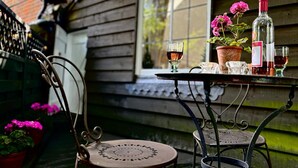 A rustic outdoor setting with a metal table and chairs, a potted plant, and a bottle of wine.