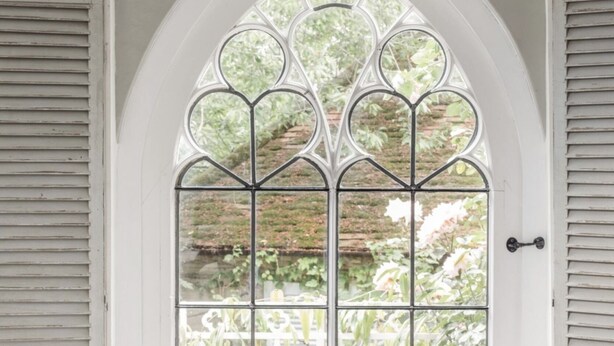A room with a white arched window, a cushioned bench, and a door with a metal gate.