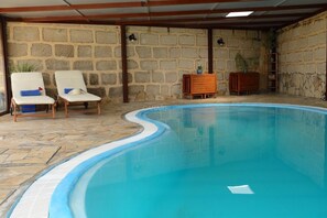 A swimming pool with lounge chairs, stone walls, and wooden furniture. - Charming Two-Bedroom Country House with Heated Pool (Arico)